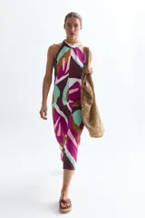 Vestido midi de lino con estampado abstracto en tonos marrón, fucsia, celeste y blanco. Tiene escote halter con detalle de collar de conchitas y cierre invisible en la espalda.