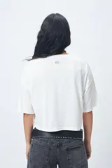 Remera blanca cropped de mangas cortas amplias con ojales metálicos a lo largo de las mangas.