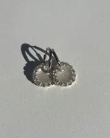 Par de aros colgantes con argolla de acero quirúrgico, dije circular de resina negra y borde de strass plateado.