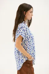 Blusa estampada con hojas azules sobre fondo blanco, con cuello en V y mangas cortas con dobladillo.