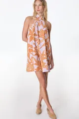 Vestido corto con estampado floral en tonos naranja sobre fondo lila, con cuello halter y corte suelto.