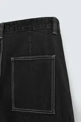 Pantalón relaxed fit de denim negro con costuras blancas en contraste, bolsillos frontales y traseros de parche, cierre frontal con cremallera y botón.
