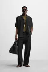 Camisa negra de corte relaxed fit, confeccionada en tejido con mezcla de modal. Tiene cuello bowling, manga corta, bolsillo de parche en el pecho y cierre frontal con botones.