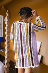 Vestido corto de tejido calado a rayas verticales en tonos blanco, lila, amarillo y borgoña, con mangas largas y terminaciones con puntilla.