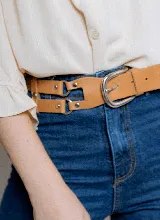 Cinturón de cuero color marrón, con hebilla metálica plateada de doble arco y detalles de remaches.