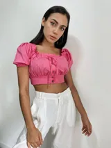 Top rosado con escote cuadrado, mangas cortas abullonadas, cierre frontal con botones y lazo ajustable en el escote.