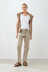 Pantalón de jean color beige, de corte recto, con bolsillos laterales y traseros. Se ajusta a la cintura con cinturón de cuero marrón.