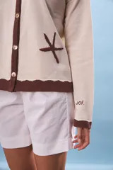 Cárdigan color crema con cuello y borde inferior marrón. Tiene cierre frontal con botones y bordados de estrellas de mar.