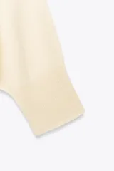 Sweater color crema de tejido de punto liso, con cuello barco y mangas anchas que se estrechan hacia la muñeca.