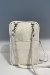 Bolso pequeño tipo bandolera o cartera de mano, confeccionado en cuero vacuno color taupe/marrón claro, con detalles en material metalizado plateado. Presenta un bordado de flor de lis en el frente y cierre superior. Incluye correa fina desmontable.