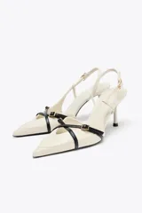 Zapato de tacón color crema con punta fina, tiras cruzadas en el empeine con hebilla dorada y tira trasera ajustable con hebilla.