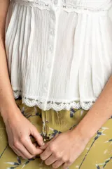 Blusa blanca de algodón con tirantes finos y escote en V. Presenta detalles de encaje en el escote y en el ruedo, y cierre frontal con botones.