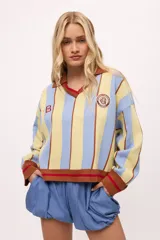 Sweater de punto color crudo con rayas verticales rojas, cuello polo marrón con borde negro, puños y ruedo acanalados en marrón y negro.