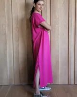 Vestido largo color crudo con cuello redondo y mangas cortas con ribete negro. Tiene corte recto y aberturas laterales en el ruedo.