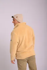 Buzo color beige de poliéster con textura tipo sherpa, cuello alto con cierre medio, bolsillo tipo parche en el pecho de color naranja con cierre vertical y puños con elástico.