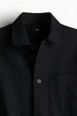 Sobrecamisa negra de manga larga con cuello inglés, tapeta lisa, canesú en la espalda y bolsillo superior de parche.