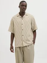 Camisa de manga corta Jack & Jones con cuello resort y cierre de botones. Diseño con estampado de espiga en tonos beige y blanco. Confeccionada en tejido dobby 100% algodón.