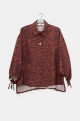Camisa marrón con estampado animal print en tonos naranja y marrón. Tiene cuello clásico, cierre con botones y mangas largas abullonadas con lazos en los puños.