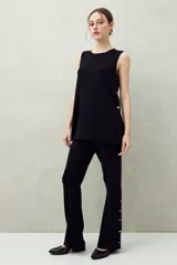 Pantalón negro de punto con calce relajado, caída fluida y botones dorados en los laterales.