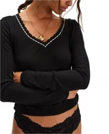 Top de manga larga ajustado de punto ligero tipo pointelle, color blanco, con escote en V ribeteado con encaje negro y blanco.