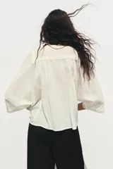 Blusa color crema de cuello redondo con escote pico y manga ancha por debajo del codo. Detalle de acabados con bordados. Cierre frontal con botones.