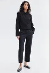 Pantalón cigarette tobillero negro con cintura estándar, cierre y pretina prolongada con corchete oculto. Piernas ajustadas con abertura corta en los bajos, bolsillos al bies y bolsillo de atrás decorativo. Pliegues adelante y atrás.
