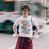 Remera blanca de algodón con corte boxy y estampado con el logo de Gurises Club, que incluye un personaje de caricatura, estrellas, un dado y la inscripción 'Montevideo Cool Kids'.