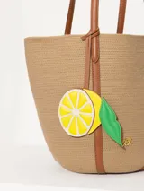 Bolso tote de hilo color beige con estructura firme y diseño espacioso. Tiene correas largas de cuero vacuno color marrón para llevar al hombro, aplique frontal de limón y logo metálico JCH.