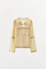 Blusa color crema de algodón y viscosa, con cuello mao y mangas largas. Presenta bordados florales con abalorios y terminaciones en puntilla. Se cierra con lazos en el frente.