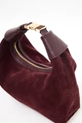 Bandolera tipo hobo de gamuza color ciruela, con correa ajustable de cuero marrón oscuro y herrajes dorados. Presenta un cierre superior con cremallera.