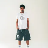 Bermuda de nylon color gris oscuro, con cintura elastizada con cordón, bolsillos laterales y bolsillos cargo con solapa. Estampado blanco con diseño de casa en la pierna izquierda.