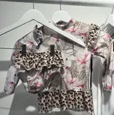 Conjunto de lycra con protección UV, estampado con flores y leopardos. Incluye remera de manga larga con cuello alto y volados, y bombacha con volados.