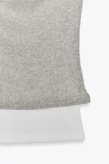 Camiseta blanca con musculosa gris superpuesta con escote asimétrico.