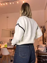 Cardigan de tejido de punto blanco y negro, con ribetes negros y apliques de flores negras bordadas con perlas y pedrería en el frente y mangas. Tiene un botón frontal.