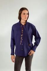 Camisa azul con cuello mao con volados, manga larga con puños con volados, cierre frontal con botones y bolsillo de parche con broche con forma de insecto.
