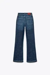 Pantalón de jean azul oscuro, de tiro alto y corte bootcut. Presenta bolsillos de parche delanteros y traseros, cierre frontal con botones y ruedo sin costuras.