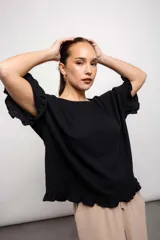 Blusa negra de corte suelto, con mangas cortas y volados en mangas y ruedo.
