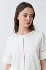 Remera blanca de manga corta con cuello redondo y detalle de vainillas en cuello, mangas y centro.
