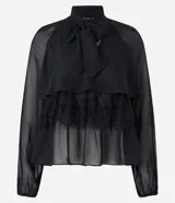 Blusa negra de chiffon con cuello alto con lazo, mangas largas con puños ajustados, detalle de volado delantero y volado en encaje.