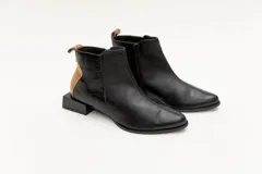 Botín corto de cuero color bronce con detalle de pieza de cuero charolada negra en el talón, cierre lateral y taco geométrico.