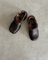 Zuecos negros de cuero con hebilla y tachas decorativas.