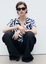 Camisa de viscosa blanca con estampado abstracto en azul, corte crop, cuello camisero, mangas cortas y nudo decorativo en el frente.