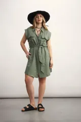 Vestido camisero corto color beige, con cuello clásico, mangas cortas con puños, dos bolsillos con solapa en el pecho, cinturón de lazo y cierre frontal con botones.