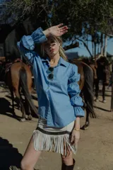 Camisa celeste de jean fino, con cuello clásico, cierre frontal con botones y mangas largas abullonadas con puños elastizados.