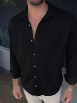 Camisa de manga larga color negro, con cuello camisero y botones marrones. El tejido parece ser lino o una mezcla con caída ligera.