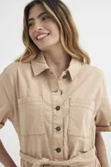 Mono corto color beige con cuello camisero, mangas cortas con dobladillo, cierre frontal con botones, cinturón de tela y bolsillos delanteros.