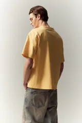 Remera de algodón color amarillo, de corte holgado, con cuello redondo ribeteado, hombros caídos y bajo recto.