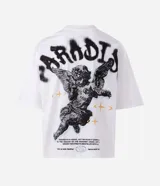 Remera blanca de algodón, corte oversized, con cuello redondo y mangas cortas. Presenta un estampado frontal con un ángel y el texto "PARADISE" en negro, y un pequeño gráfico de estrella/brújula en el lado izquierdo del pecho.