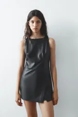 Mono corto negro de efecto piel, con cuello redondo y sisa. Presenta un corte cruzado en el delantero, costuras marcadas y cierre trasero con cremallera.