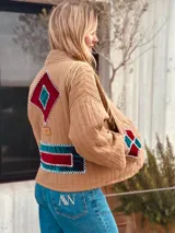 Campera capitoneada color beige con figuras geométricas bordadas a mano en terciopelo rojo y verde.